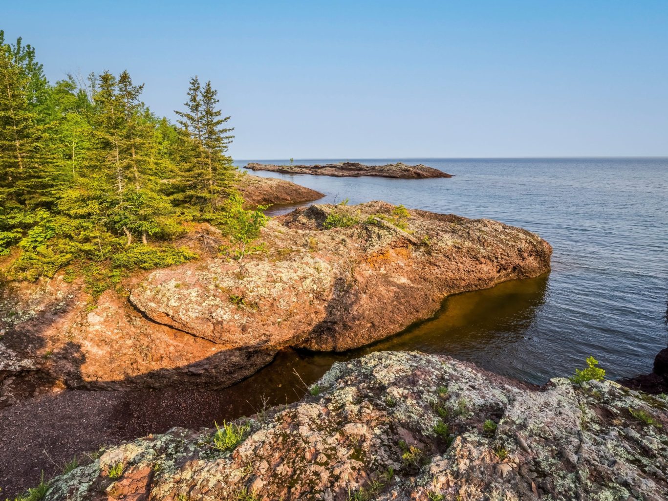 Rocky lakefront and pine trees on a sunny day near Magnuson Hotel Copper Crown.