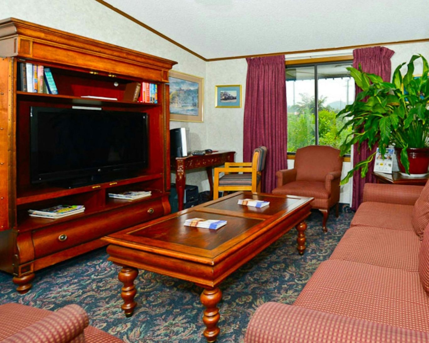 Comfortable hotel lobby with classic wooden furniture, flat-screen TV, seating area, and large window with natural light.