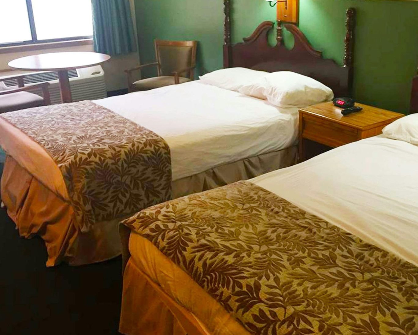 Hotel room with two double beds, patterned bed runners, wooden headboards, and a seating area near the window.