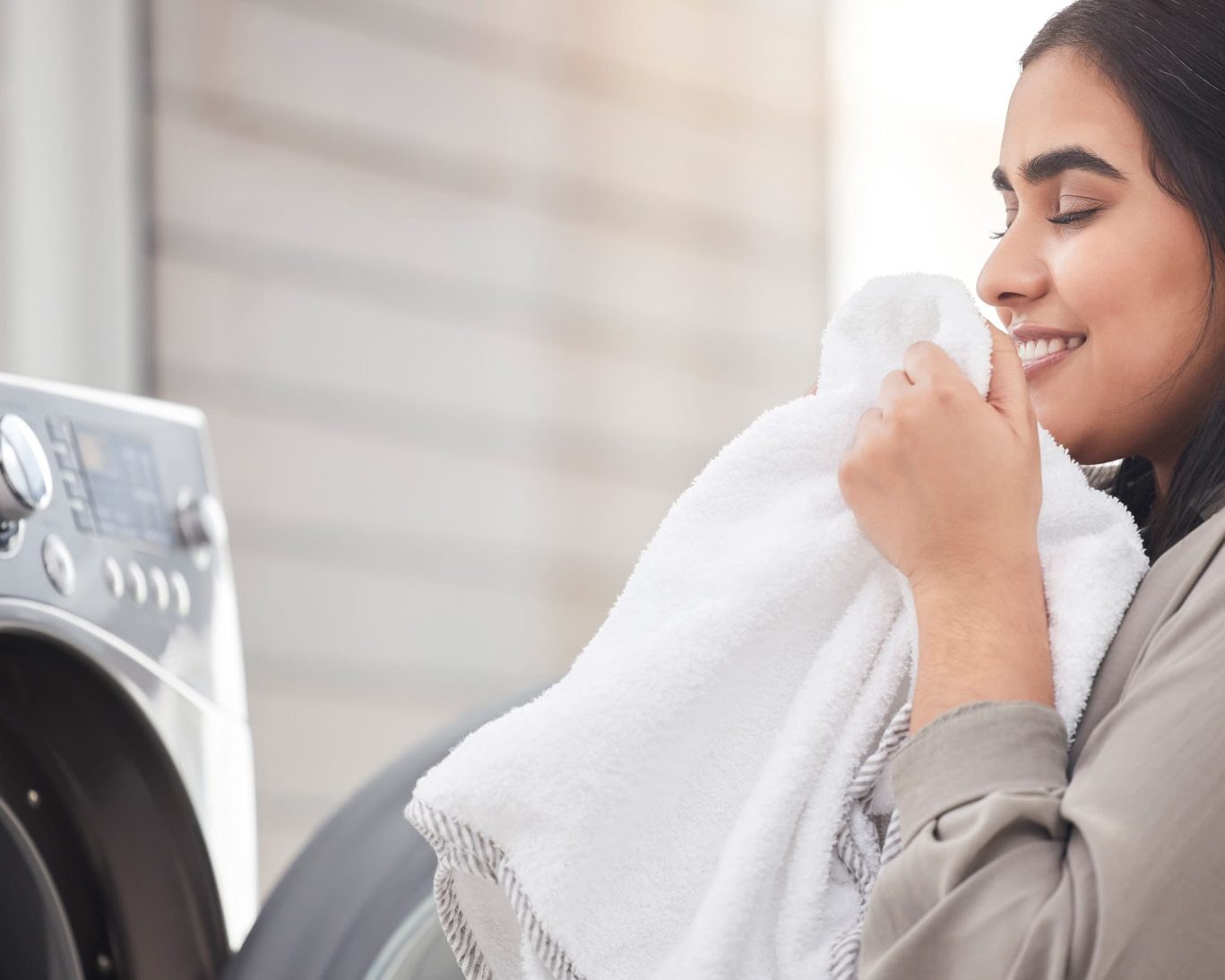 Smiling woman enjoying the fresh scent of clean white laundry in front of a washing machine.