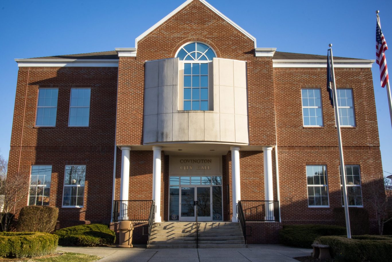 Brick Covington City Hall building with American flag and white columns under blue sky.