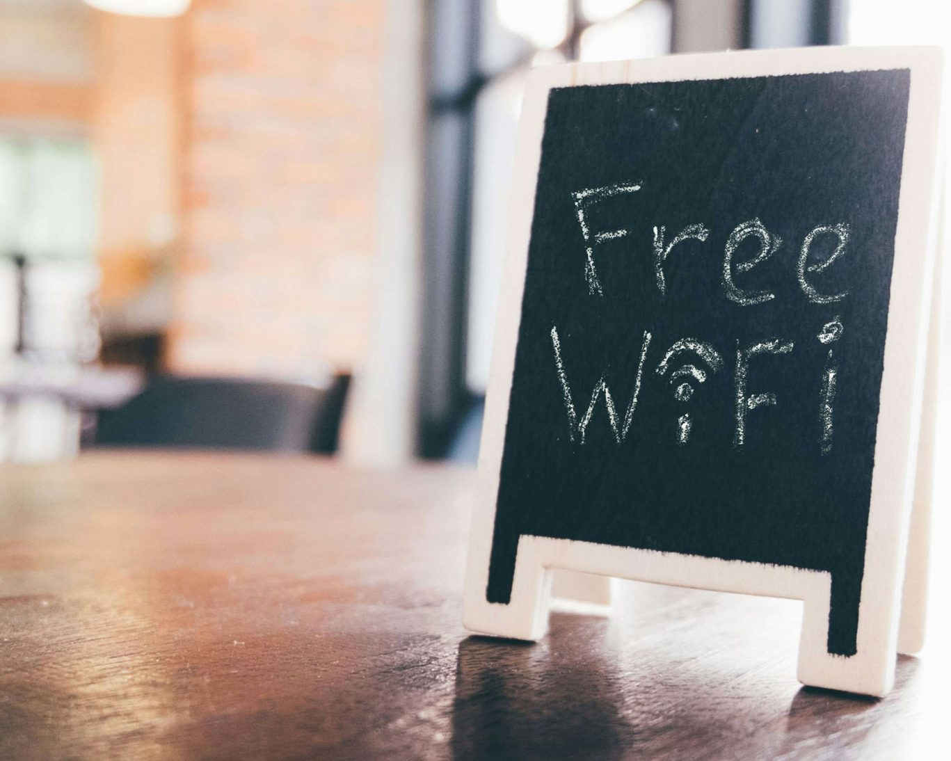 Chalkboard sign on wooden table displaying free Wi-Fi in cozy hotel lounge or café setting.