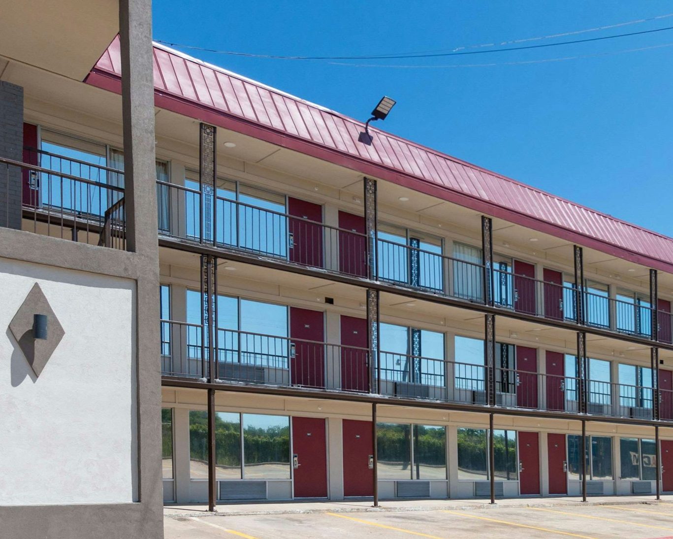 Three-story budget hotel exterior with red doors and outdoor corridors under clear blue sky.
