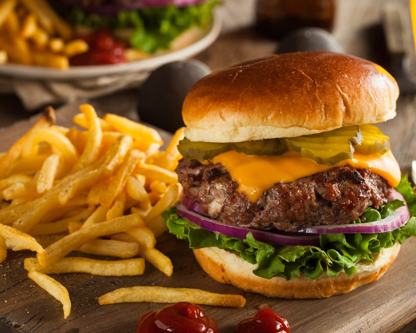 Juicy cheeseburger with pickles, onions, and fries served on a rustic wooden table