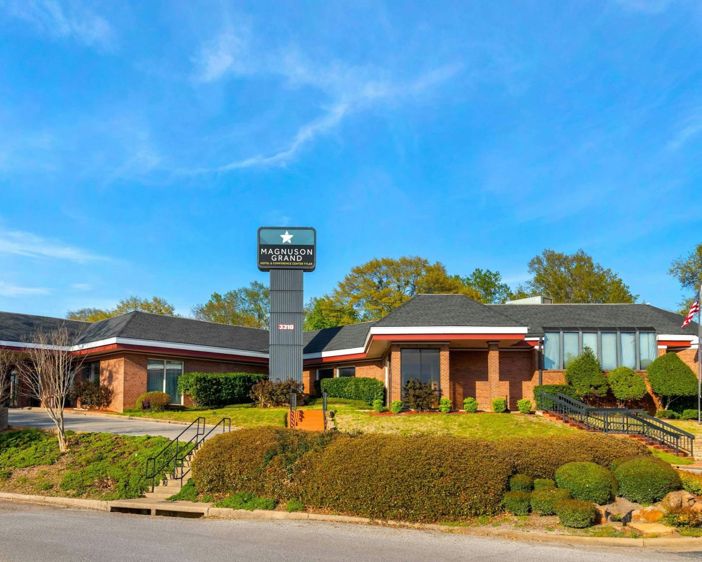 Magnuson Grand Hotel exterior with manicured landscaping and clear blue sky.