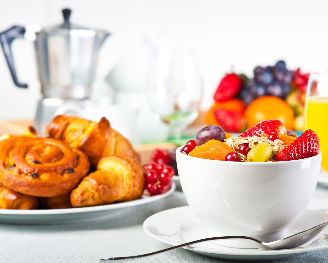 Continental breakfast with fresh fruit bowl, croissants, and orange juice.