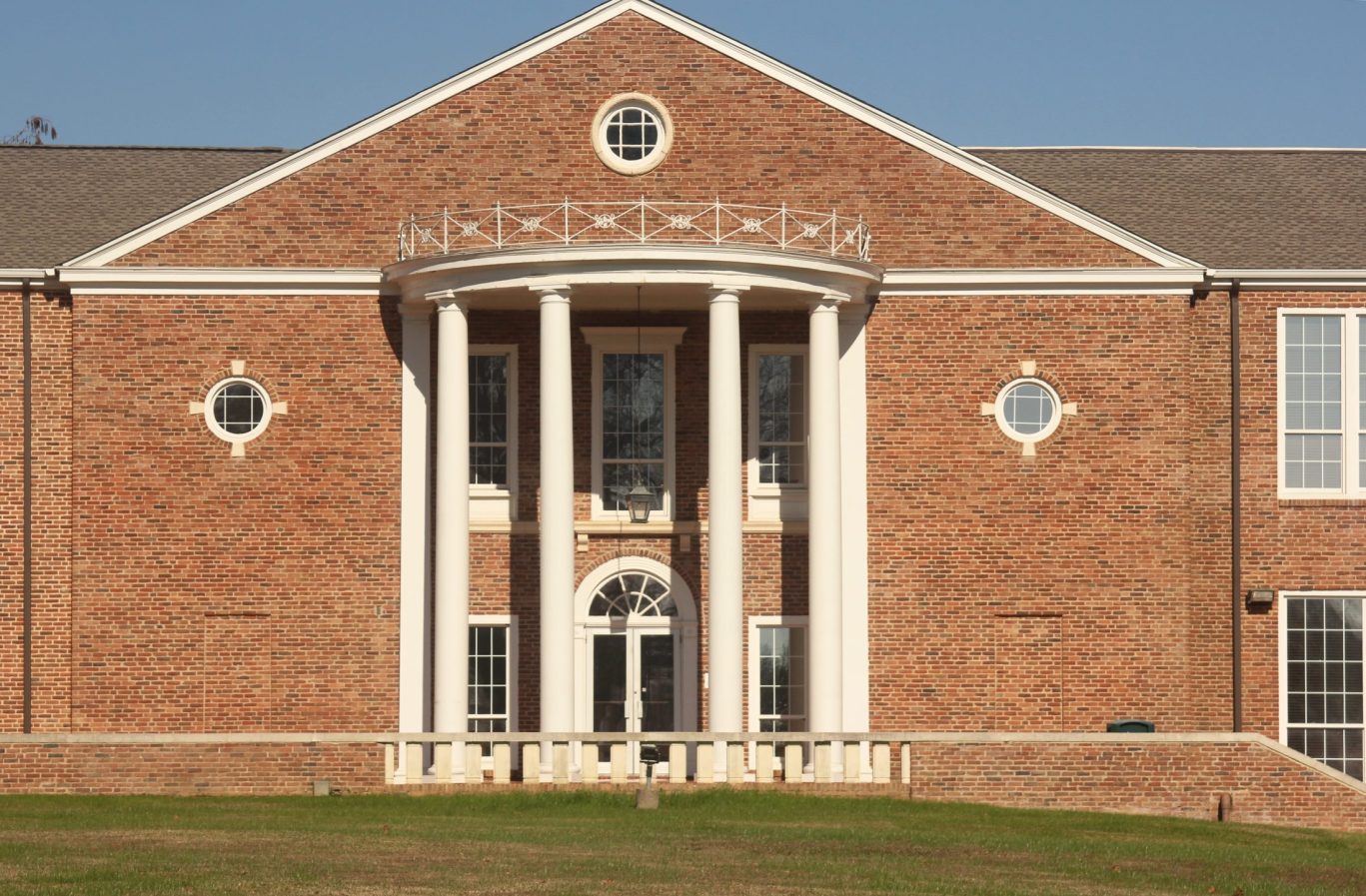 Red brick building with neoclassical white columns and symmetrical circular windows.