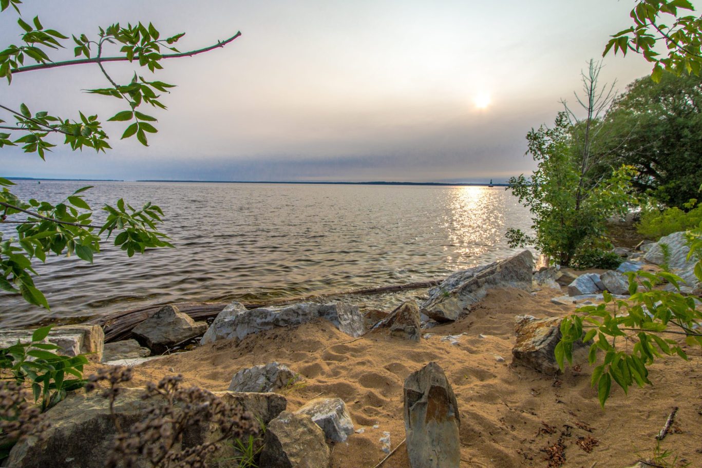 Peaceful lakeside view with rocky shoreline and gentle waves under a glowing evening sky in Jamestown.