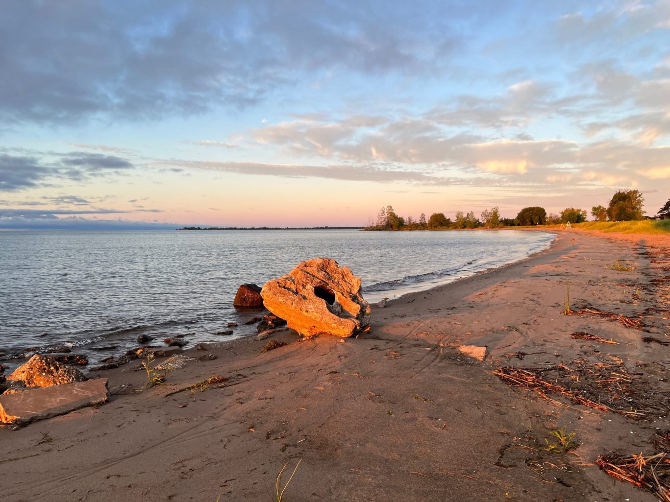 Scenic Jamestown beach during sunset with warm-toned sand, scattered rocks, and tranquil water.