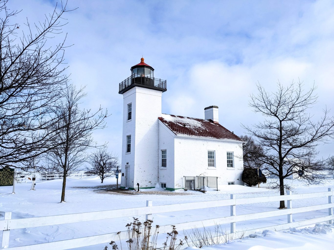 Historic white lighthouse in Jamestown surrounded by snow-covered landscape and bare trees in winter.