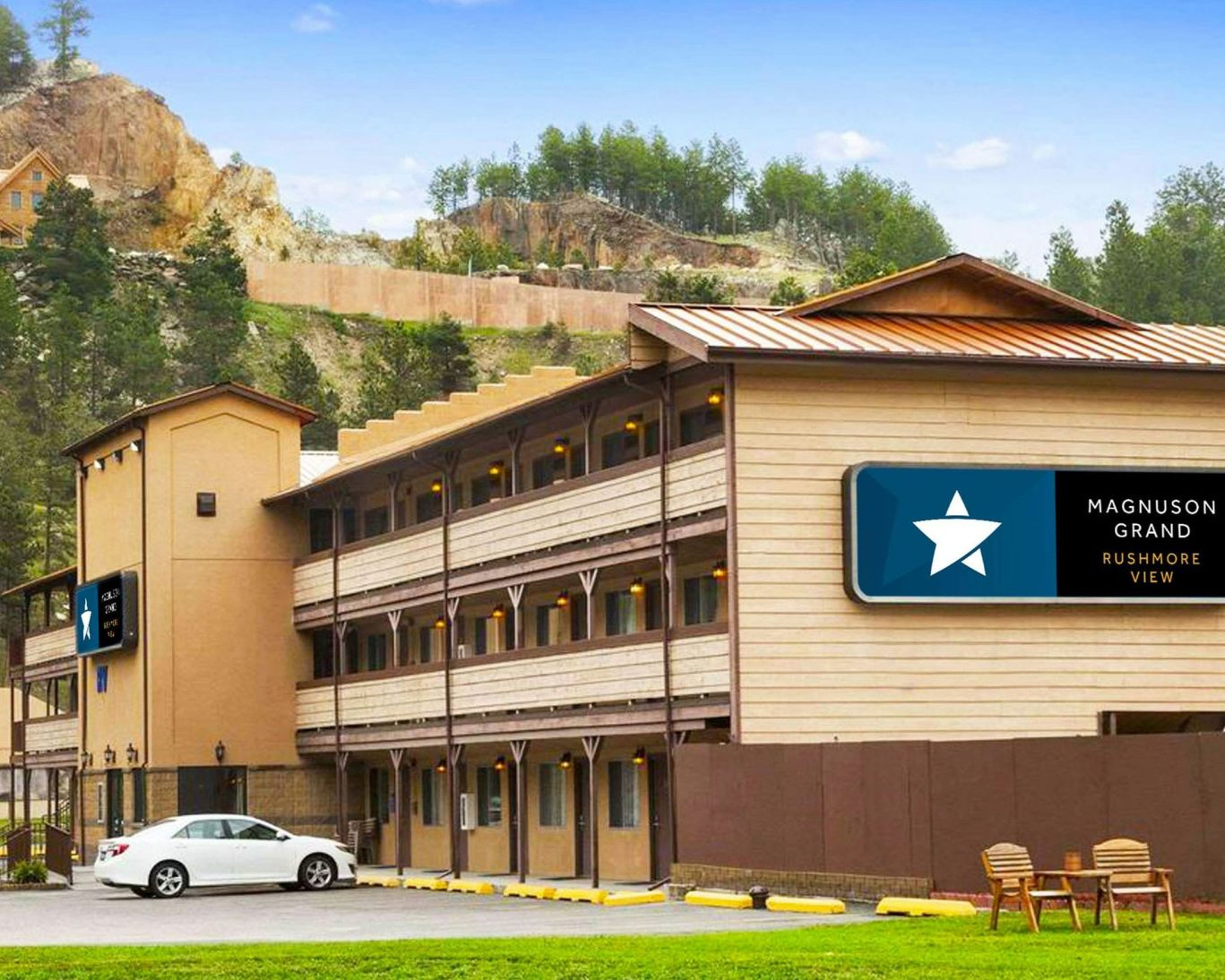 Exterior view of Magnuson Grand Rushmore View hotel with parking and scenic hillside backdrop in Keystone, South Dakota.