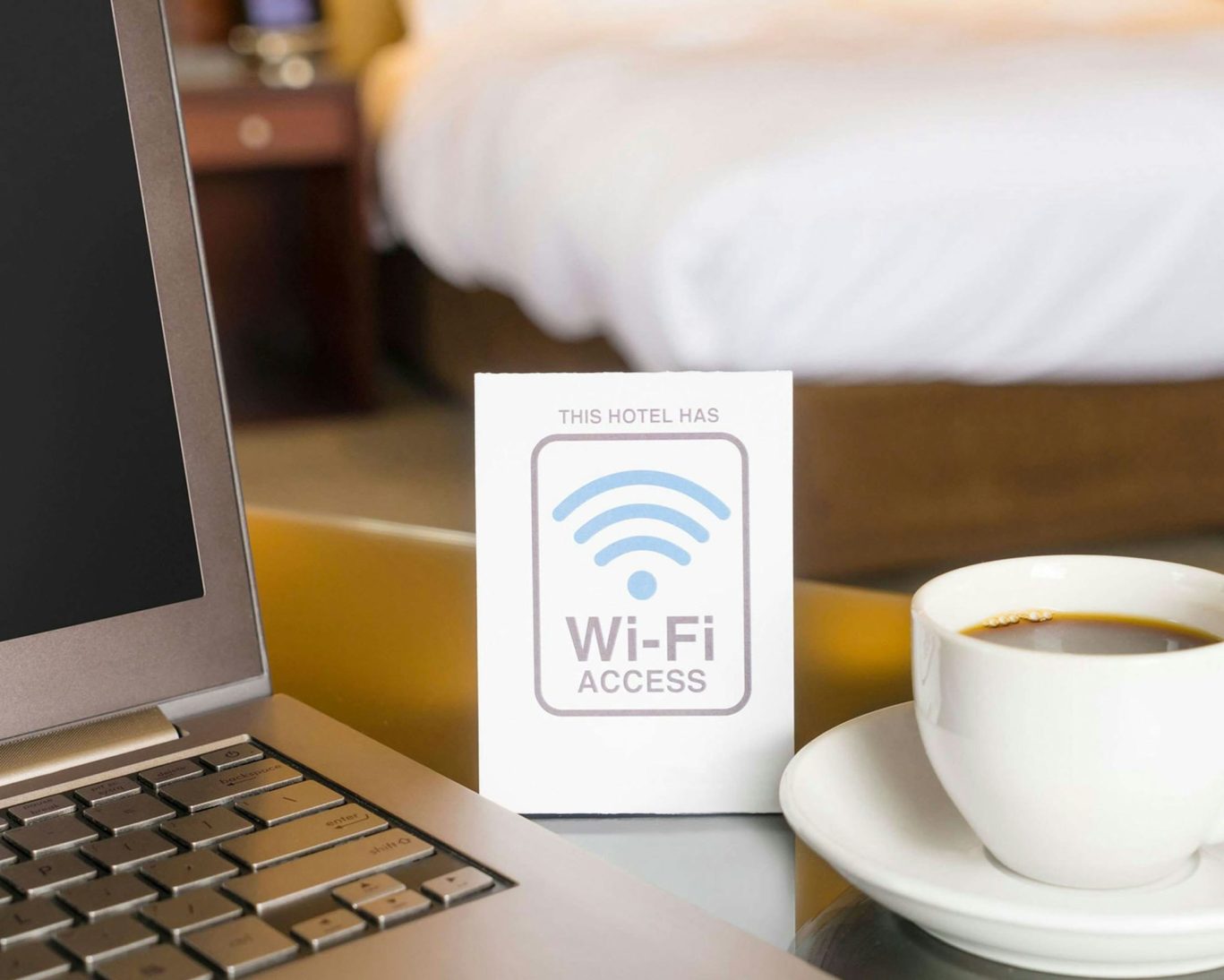 Hotel workspace with free Wi-Fi sign, coffee cup, and laptop in a comfortable guest room setting.