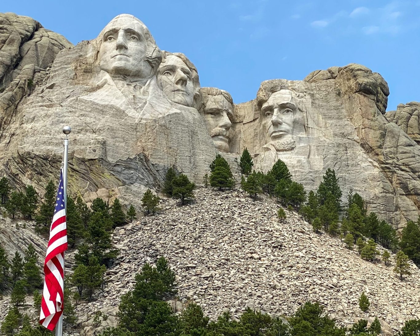 Close-up of Mount Rushmore National Memorial with American flag and clear blue sky.