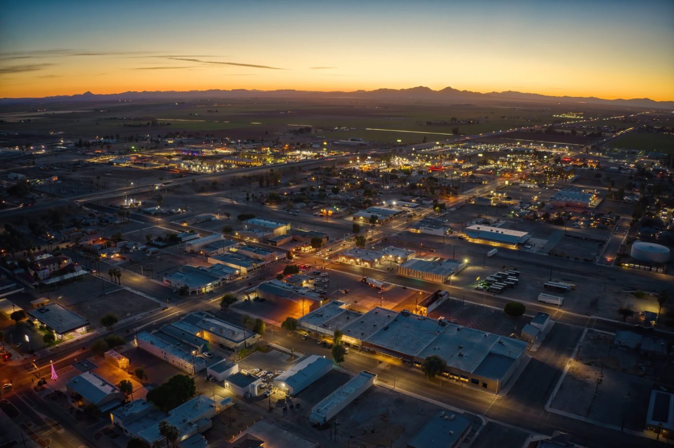 Aerial view of Blythe, California at sunset with city lights and distant mountains.
