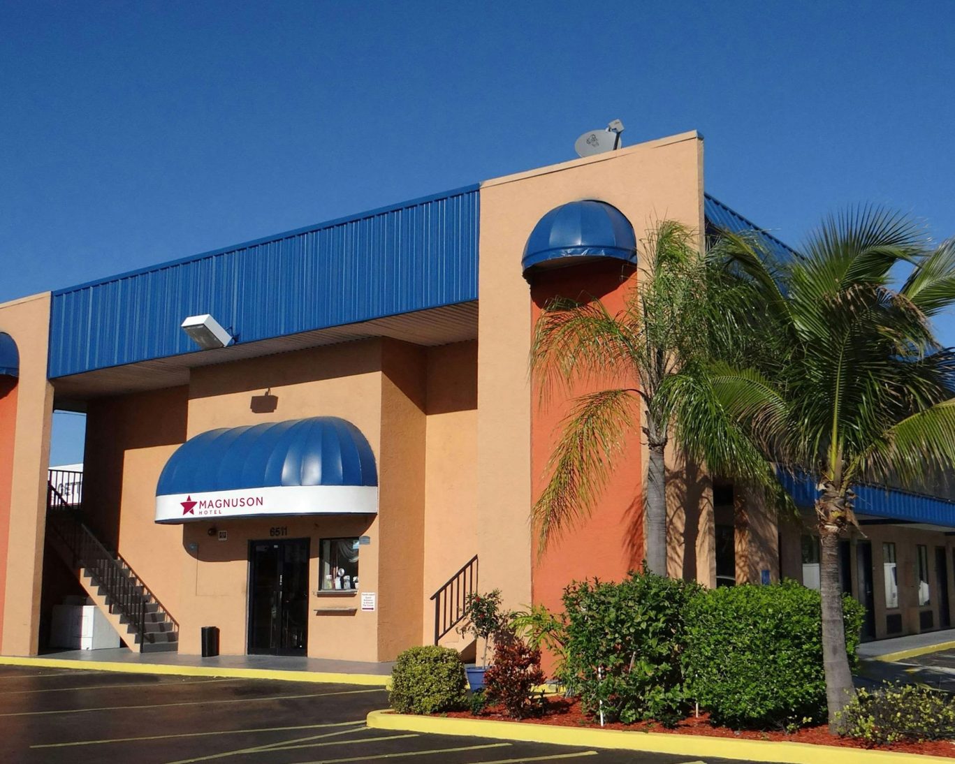 Exterior of Magnuson Hotel with palm trees and vibrant blue sky in the background.