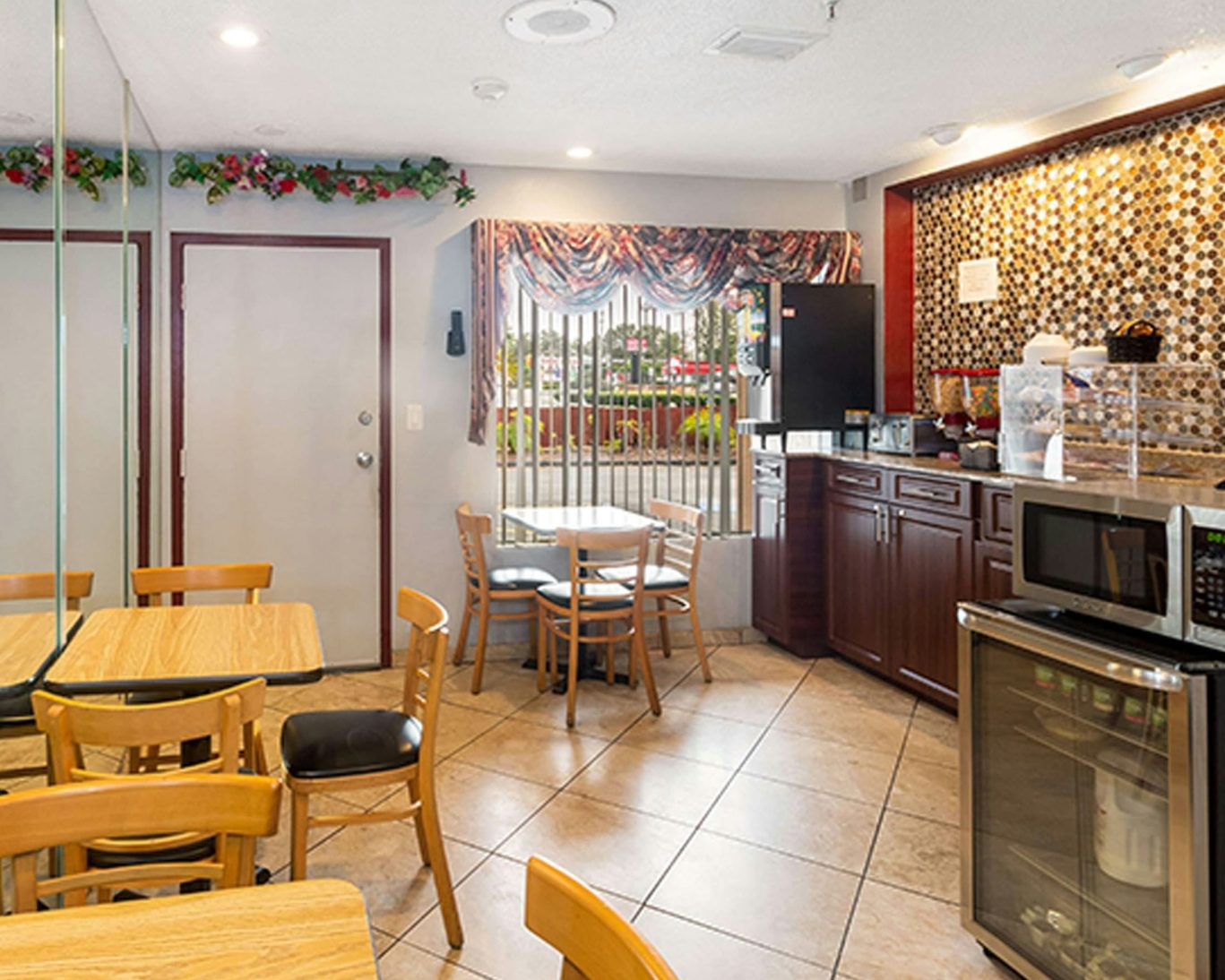 Cozy breakfast area at Magnuson Hotel with wooden tables, chairs, and self-service coffee station.