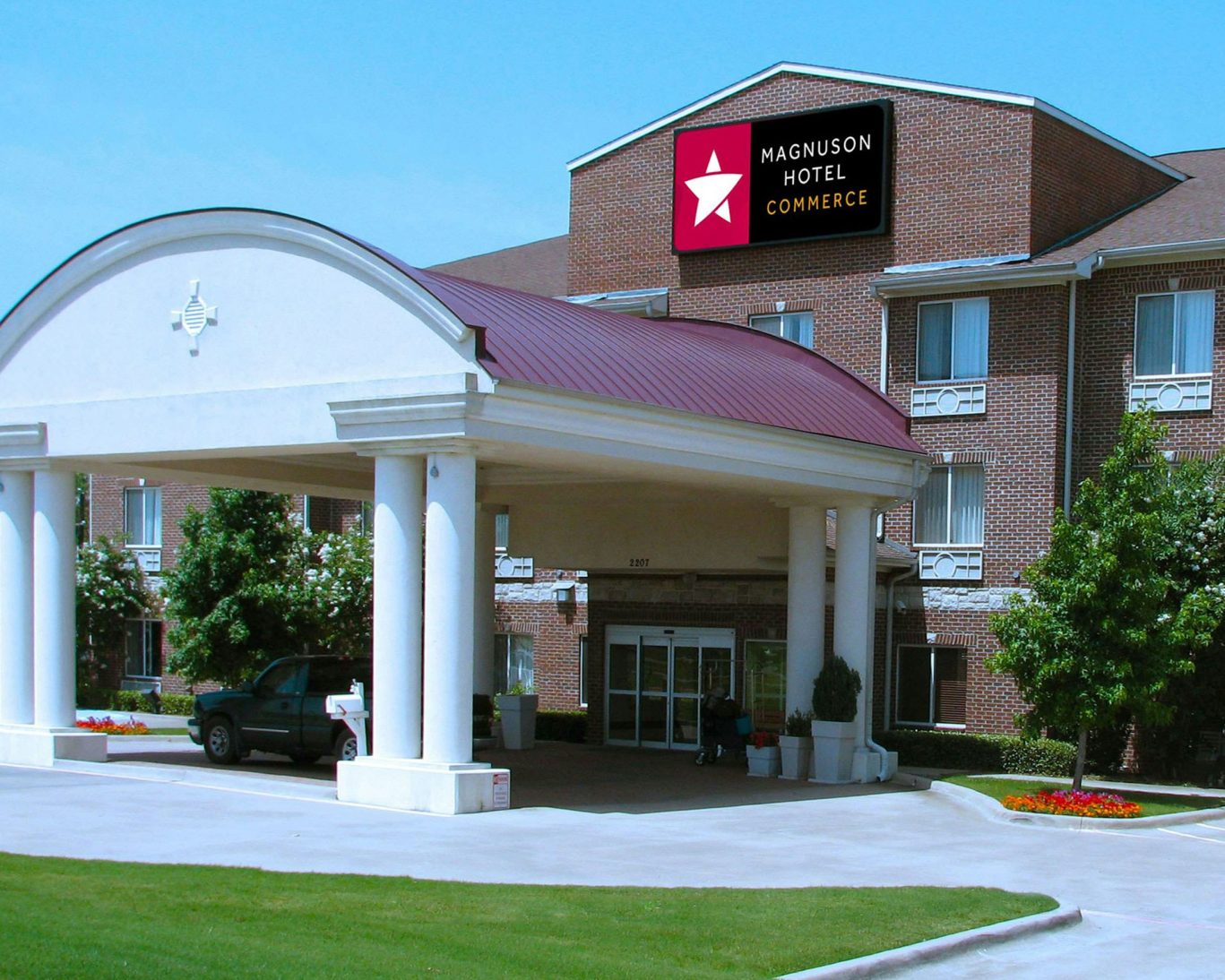 Front view of Magnuson Hotel Commerce with covered entrance and red roof on a sunny day.