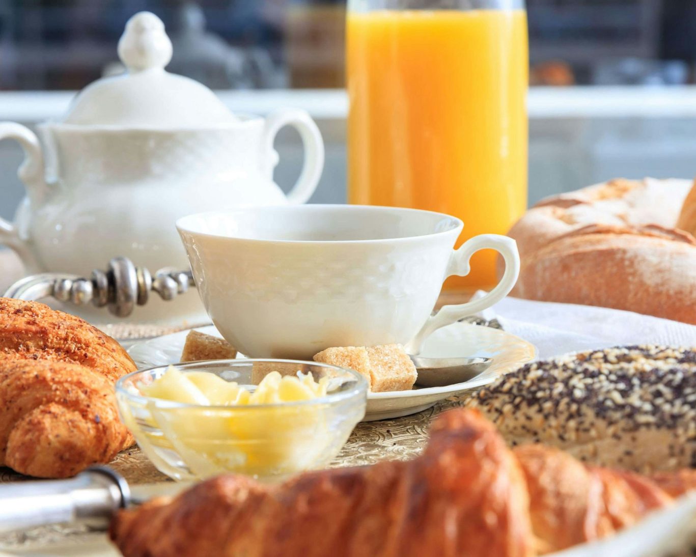 Close-up of continental breakfast with croissants, orange juice, tea set and fresh bread.