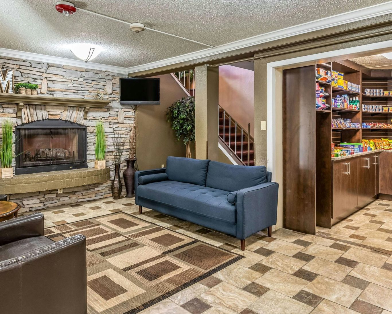 Hotel lobby with stone fireplace, blue sofa, and snack market at Magnuson Hotel Detroit.