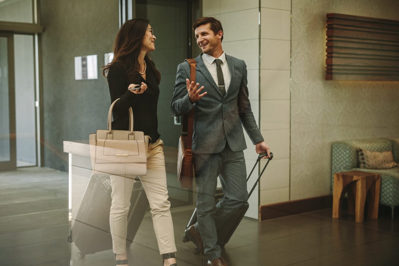 Businesswoman and a businessman checking into modern hotel lobby with suitcase.
