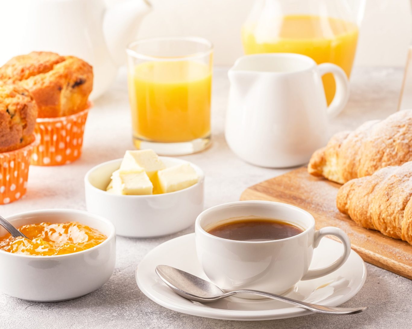 Fresh continental breakfast with coffee, croissants, muffins, butter, and orange juice.