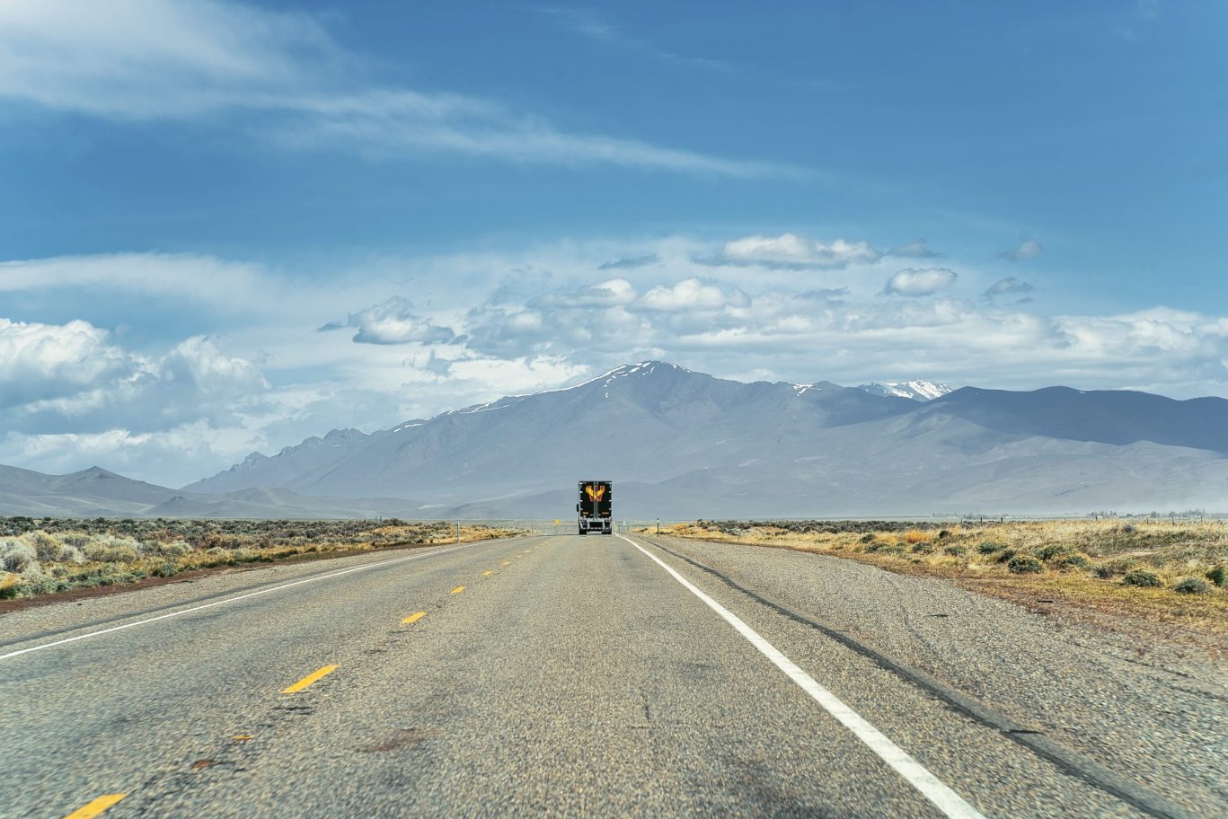 Scenic open highway leading toward distant snow-capped mountains under a blue sky in Nevada.