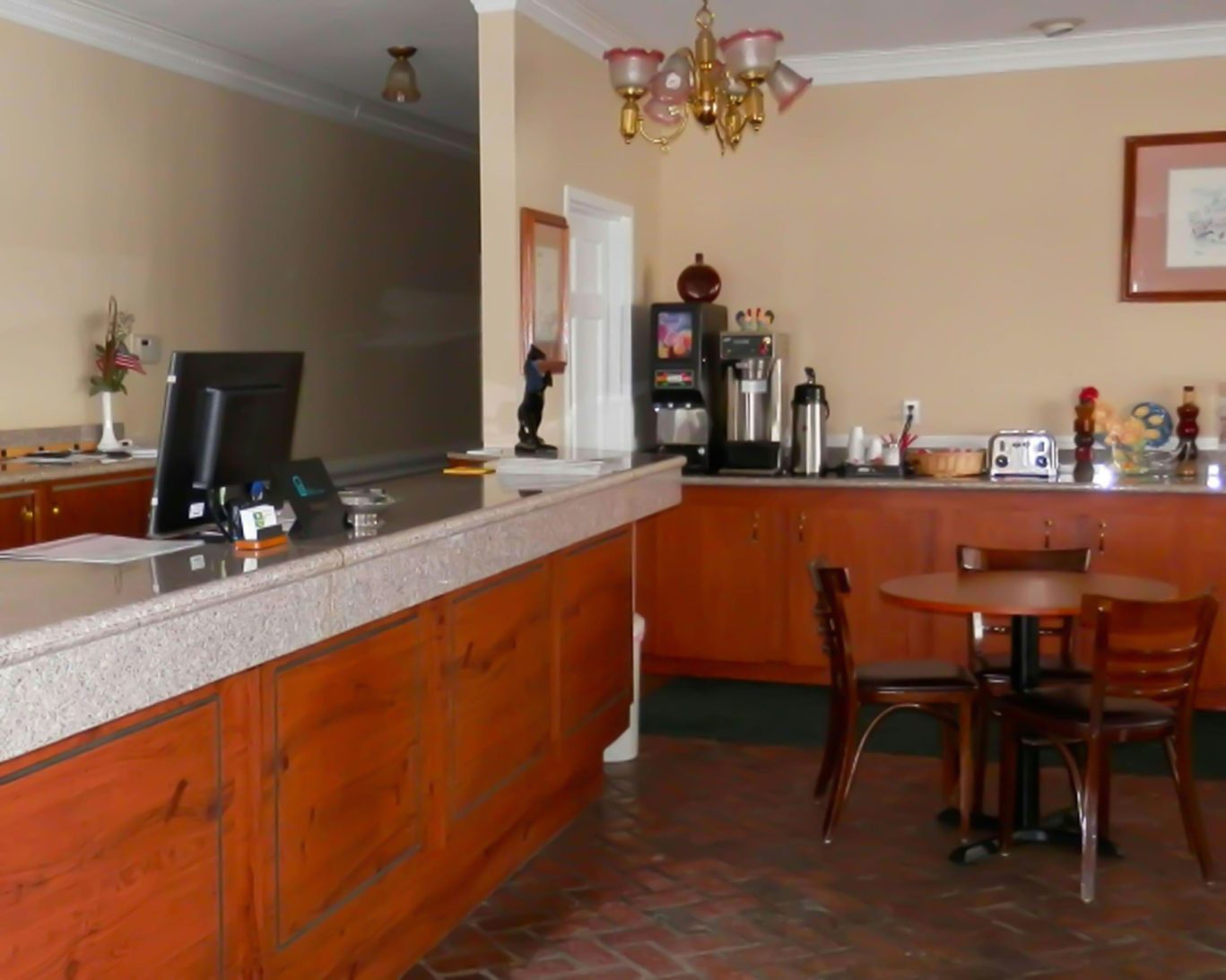 Magnuson Hotel Fowlerville front desk with adjacent breakfast seating and beverage station.