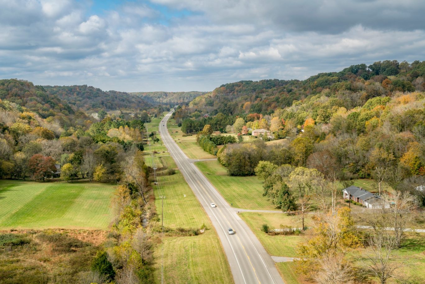 Open road cutting through a scenic green Michigan countryside with forested hills.