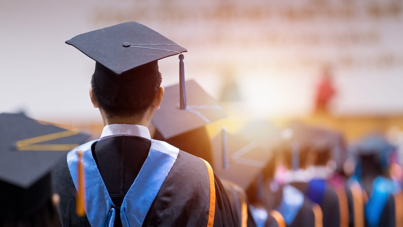shutterstock_2268966413 – Rear view of university graduates wearing graduation gown and cap in the commencement day