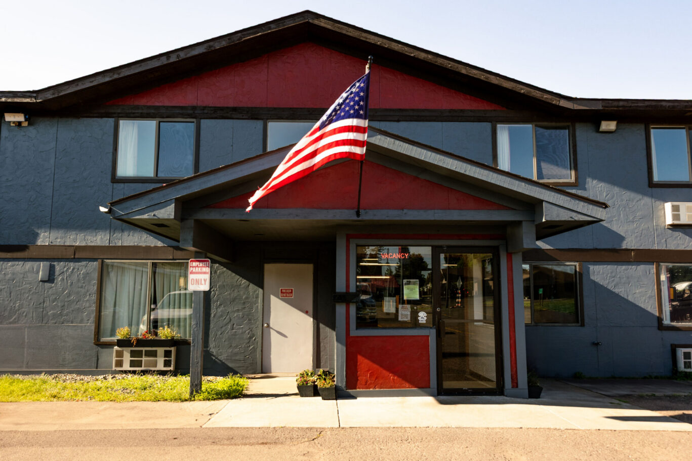 Main entrance of Magnuson Hotel with American flag, accessible parking, and hanging flower baskets.