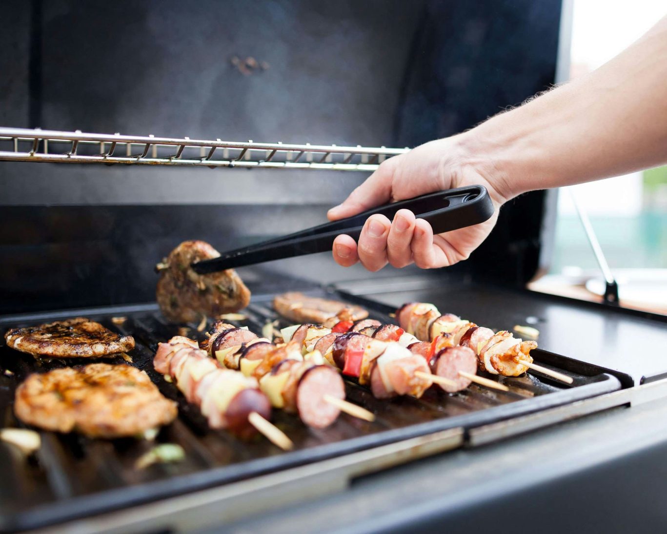 Outdoor grill with sizzling skewers and seasoned meats at Magnuson Hotel barbecue area.