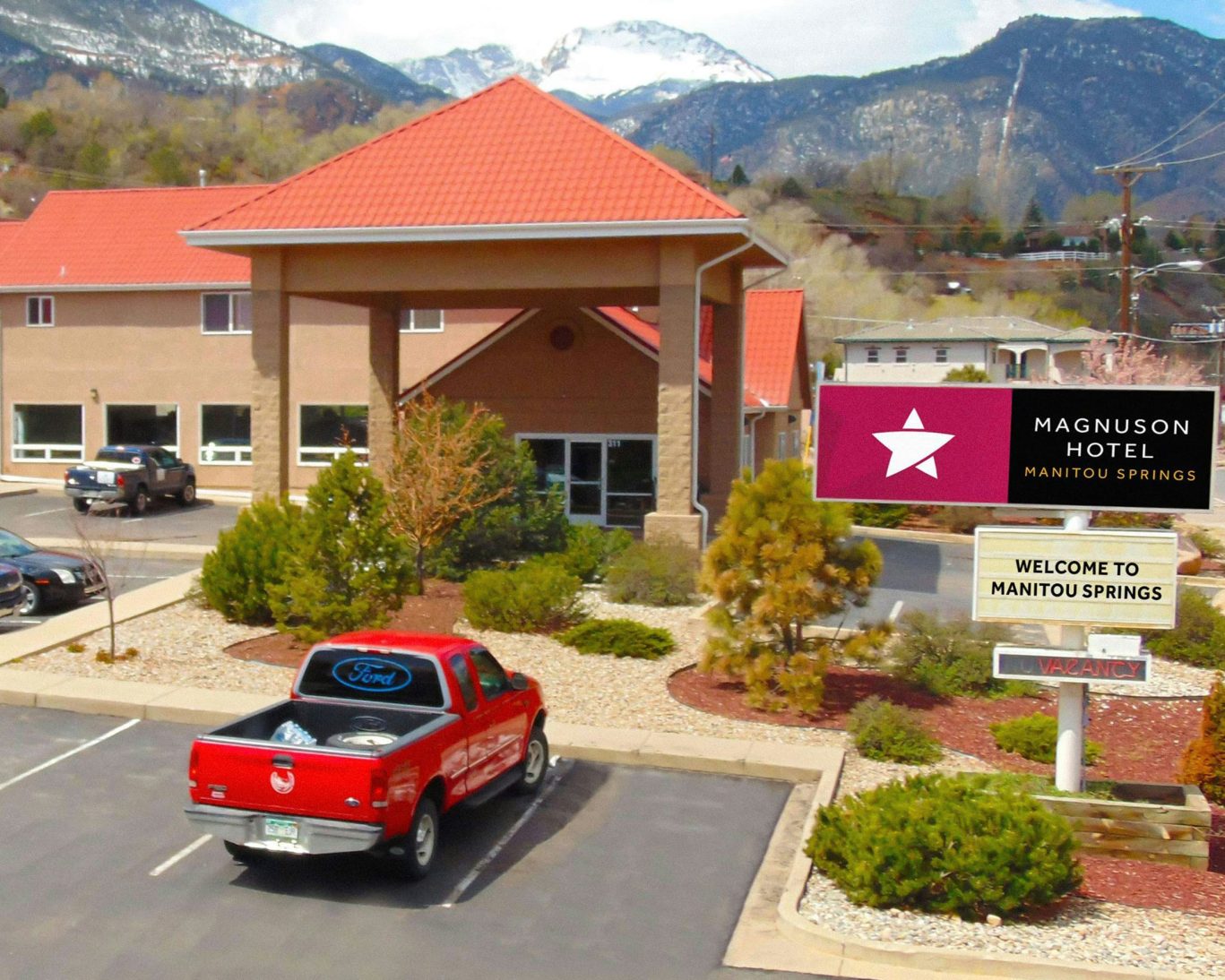 Magnuson Hotel Manitou Springs exterior with parking lot, red Ford truck, and scenic mountain view.