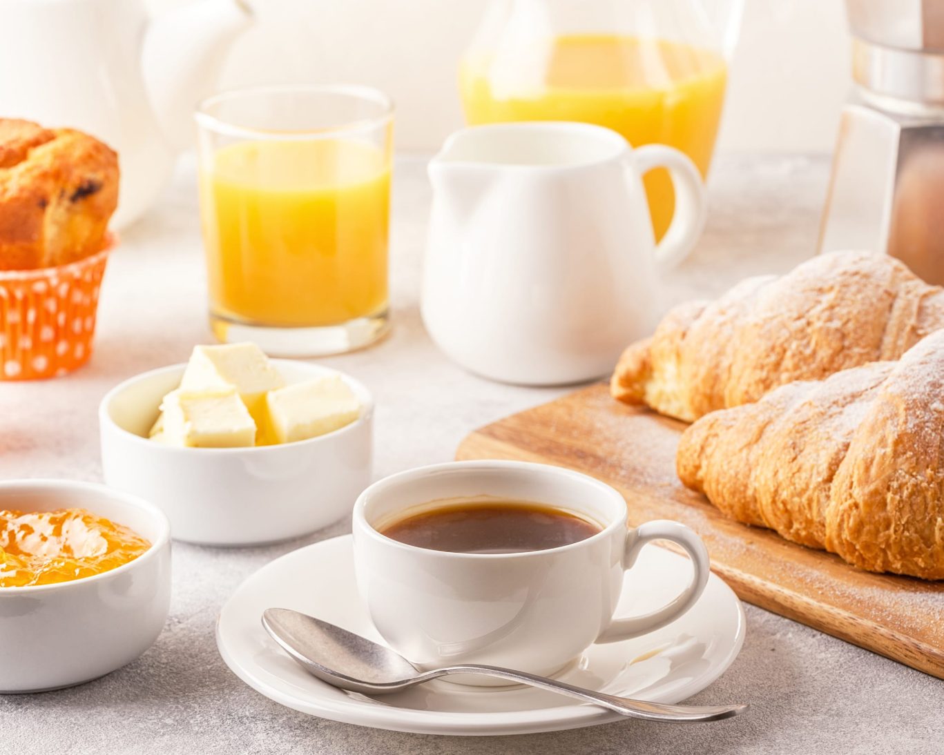 Close-up of continental breakfast with coffee, croissants, orange juice, butter, and jam.