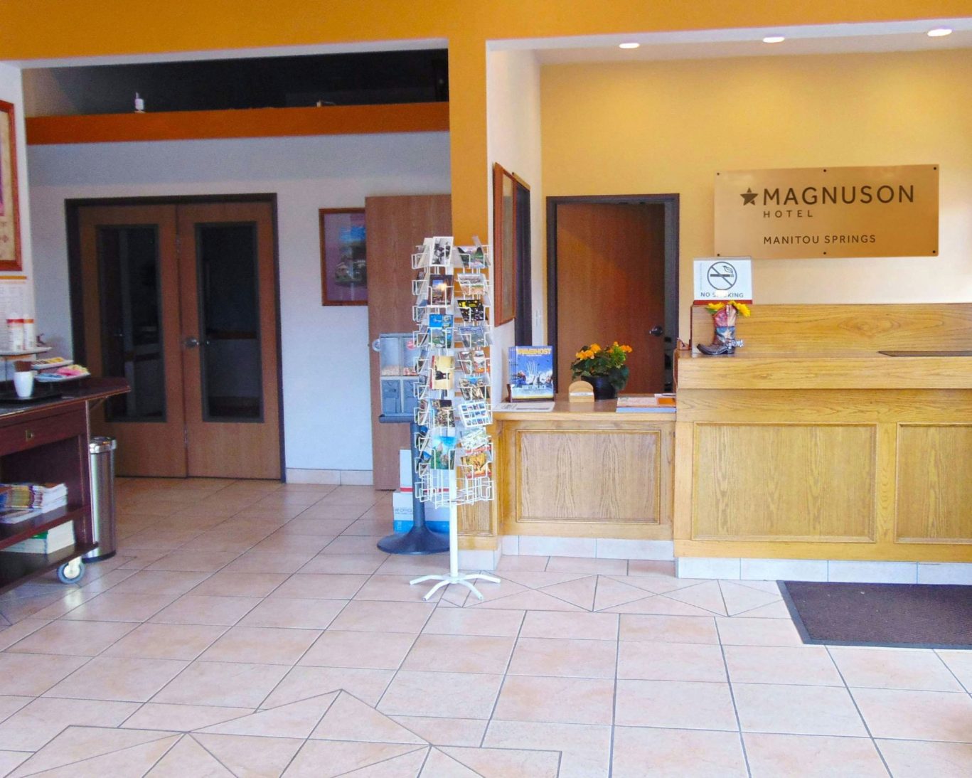 Magnuson Hotel Manitou Springs front desk and reception area with postcard rack and tiled flooring.