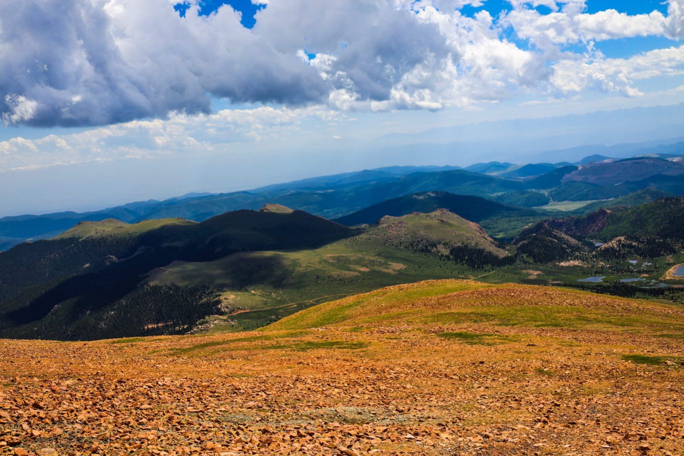 Panoramic view from Pikes Peak summit overlooking rugged Rocky Mountain landscape under cloudy sky.