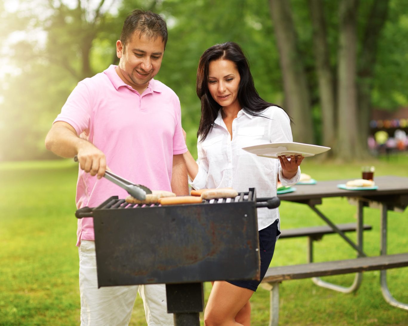 Couple enjoying a sunny day grilling hot dogs at a picnic park.