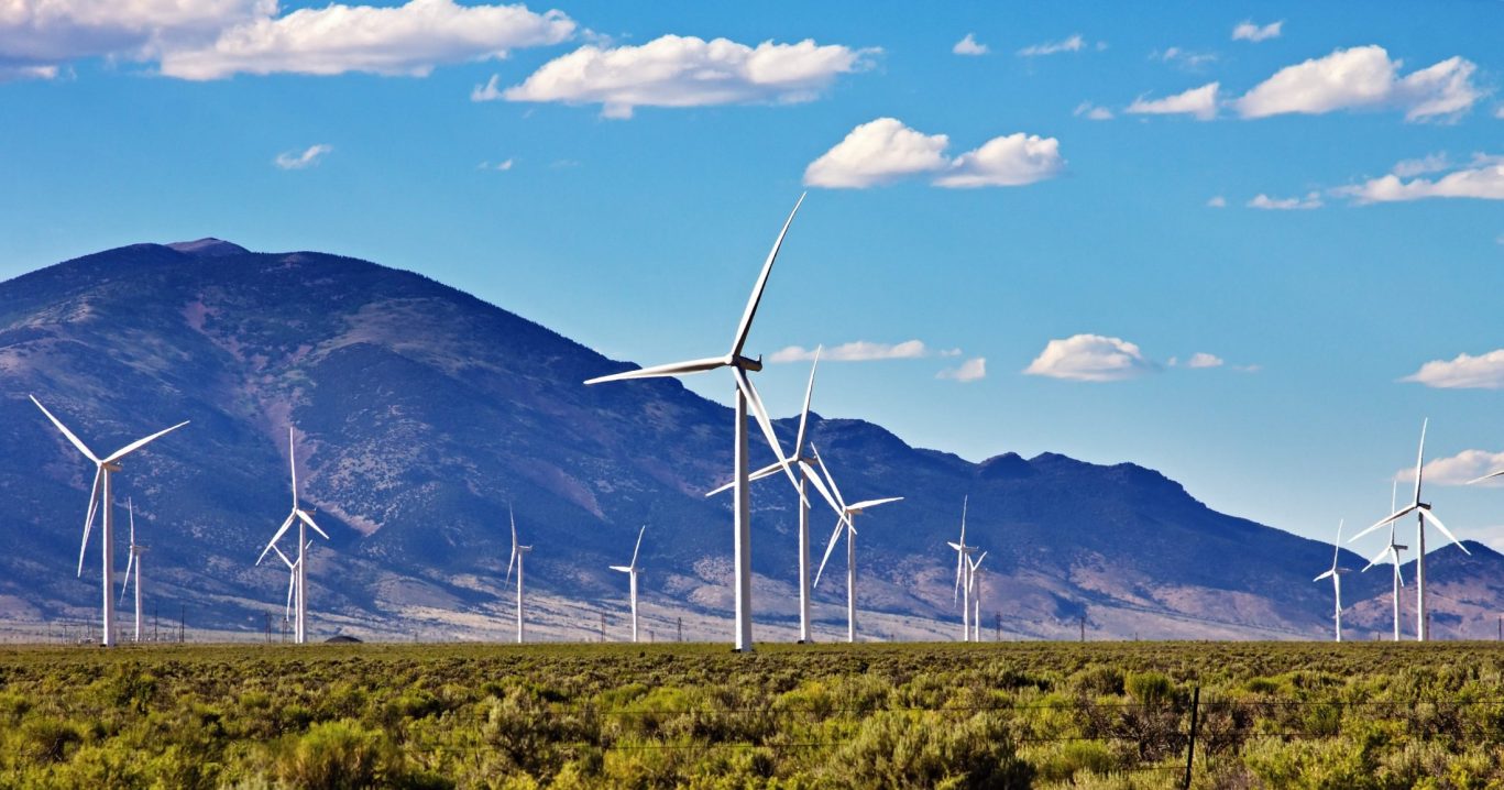 Wind turbines on a sunny day in the Nevada desert with mountain backdrop.