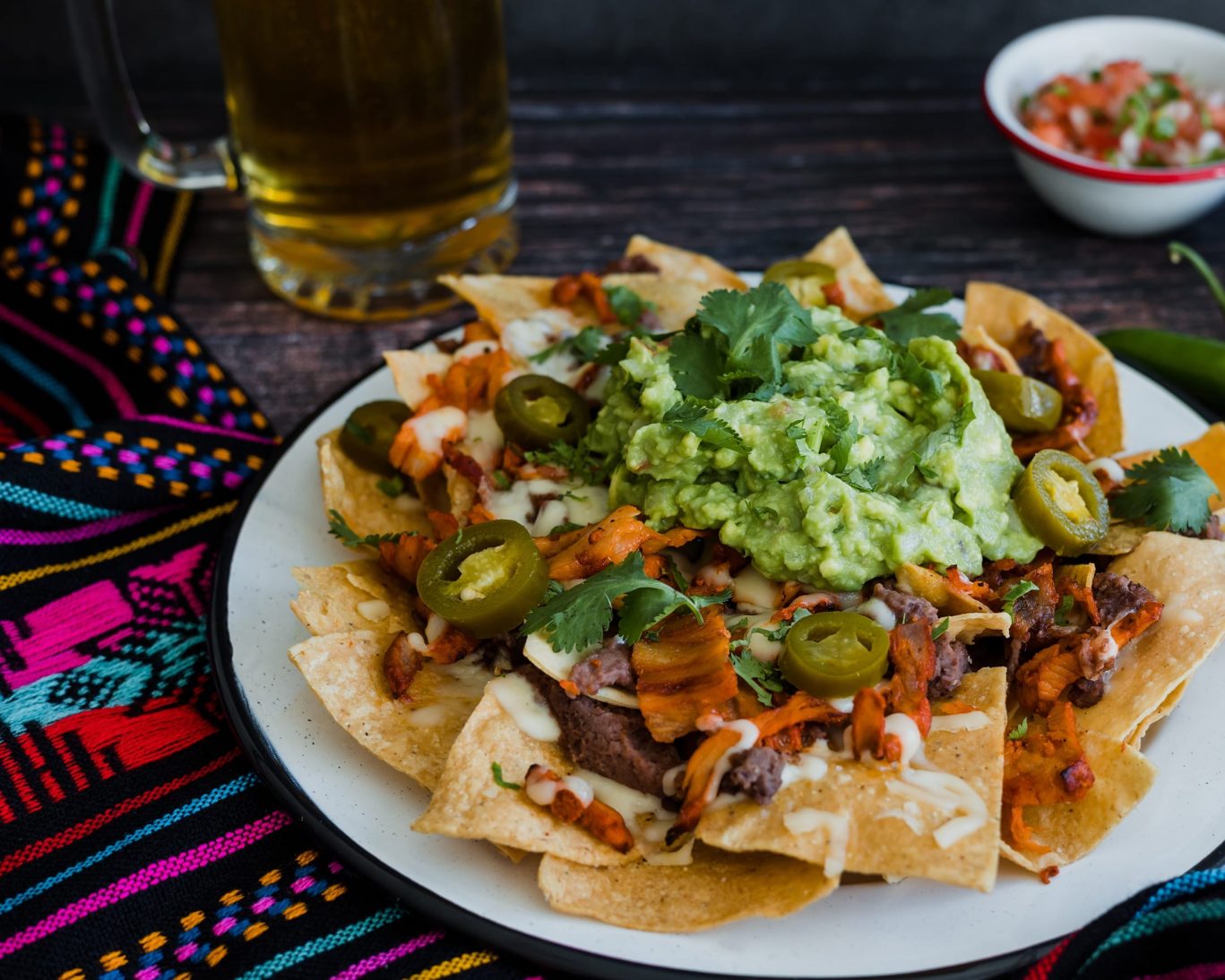 Plate of loaded nachos topped with guacamole, jalapeños, and melted cheese.
