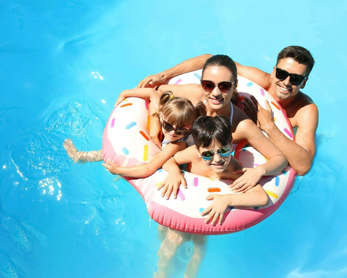Smiling family enjoying summer in pool with colorful donut float.