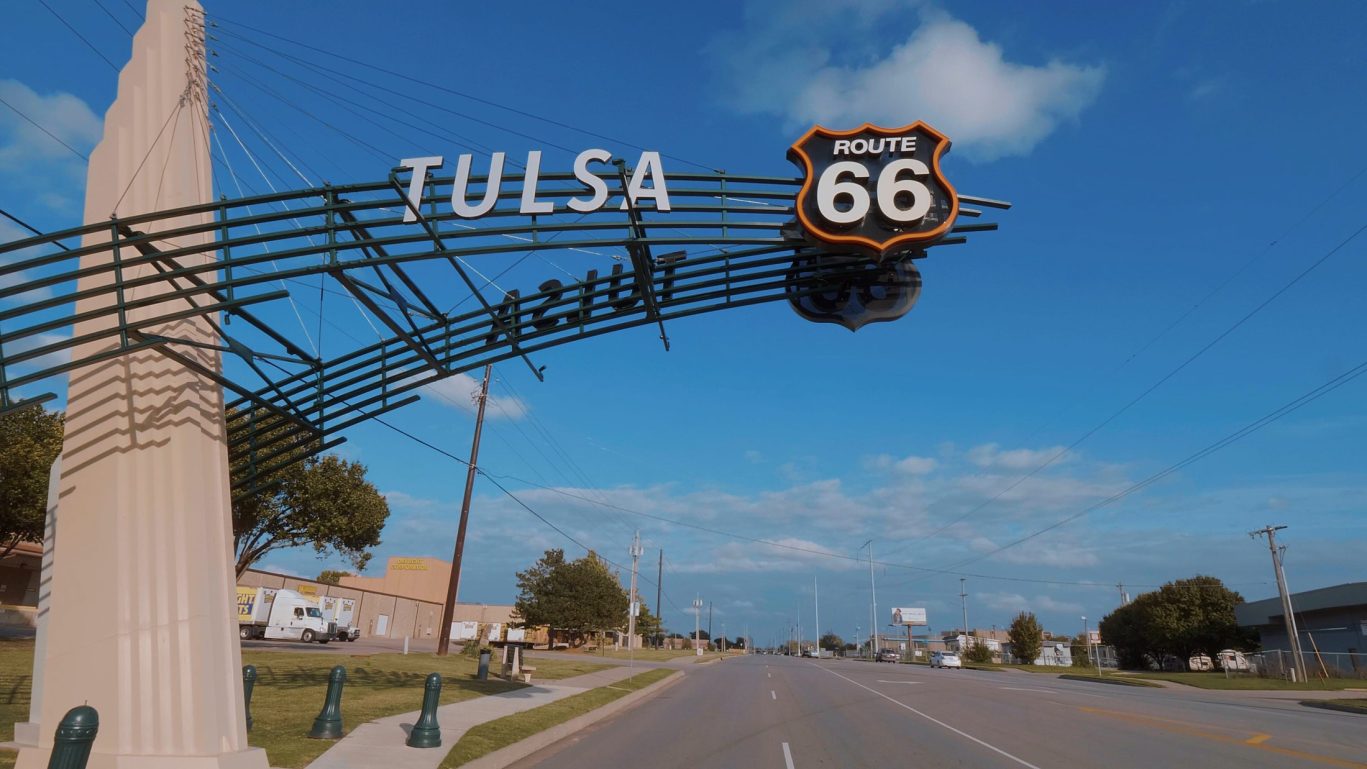 Tulsa Route 66 highway sign arching over main road with clear sky.