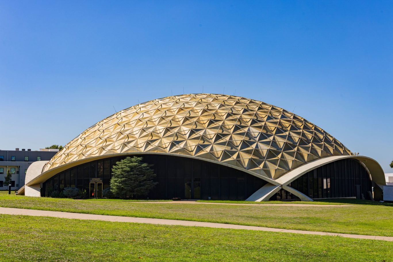 Golden geodesic dome of the Howard Auditorium against clear blue sky.