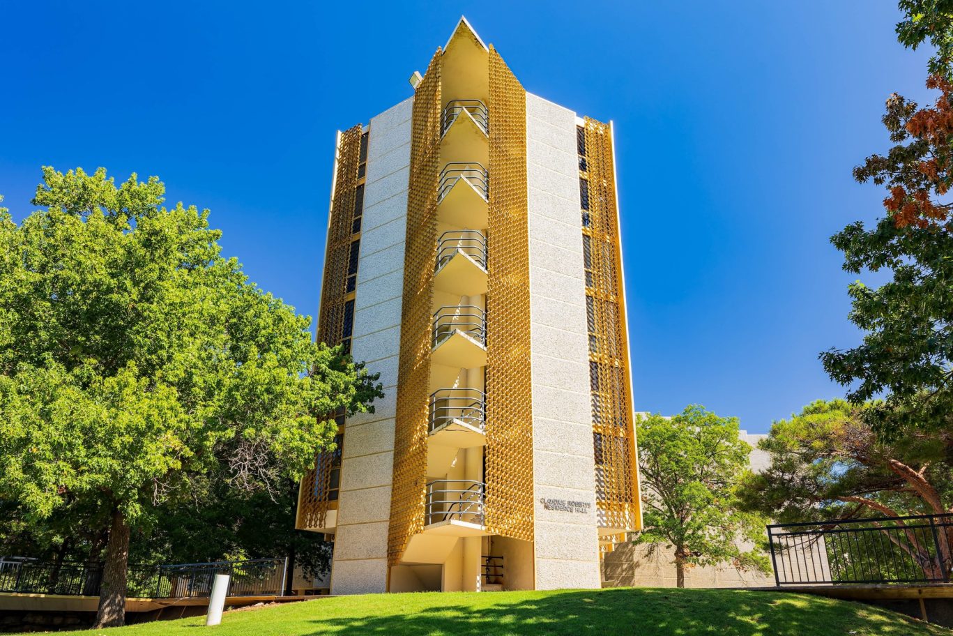 Tall Clarence Roberts Residence Hall with gold architectural accents surrounded by trees.
