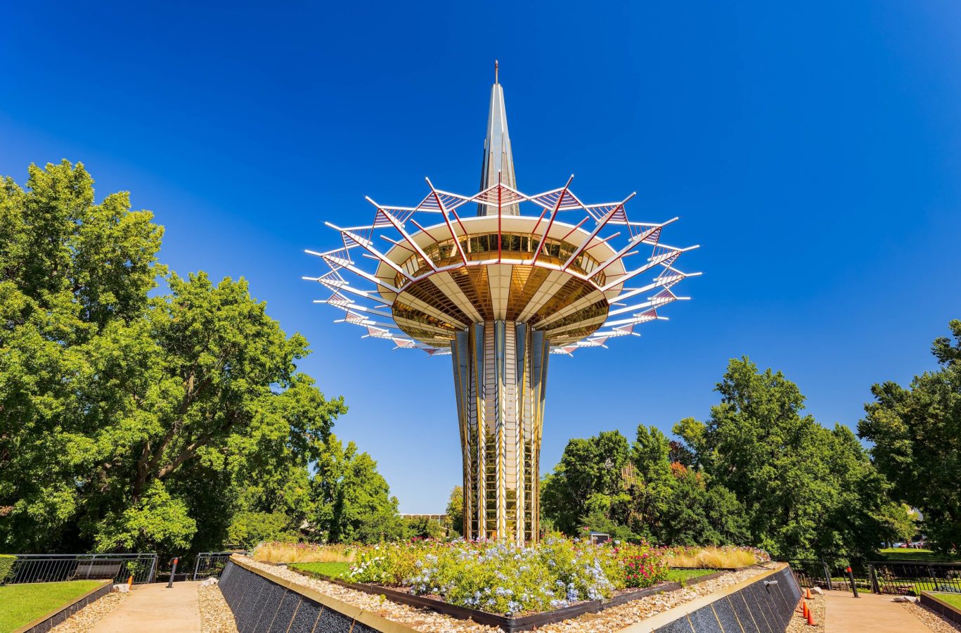 Unique tower structure in Tulsa with flower garden and bright blue sky.