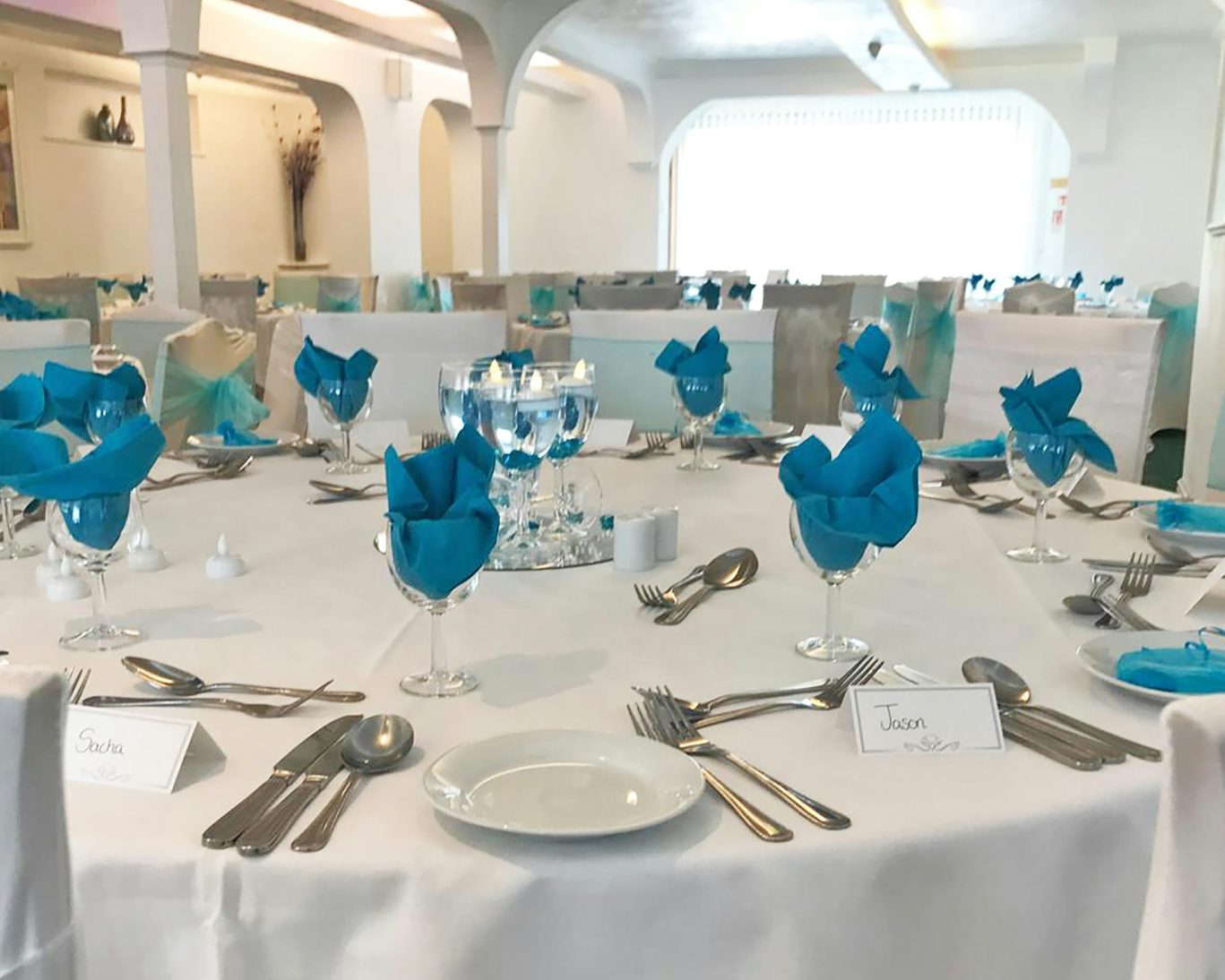 Elegant wedding or event banquet hall with round tables, blue napkins, and formal place settings.