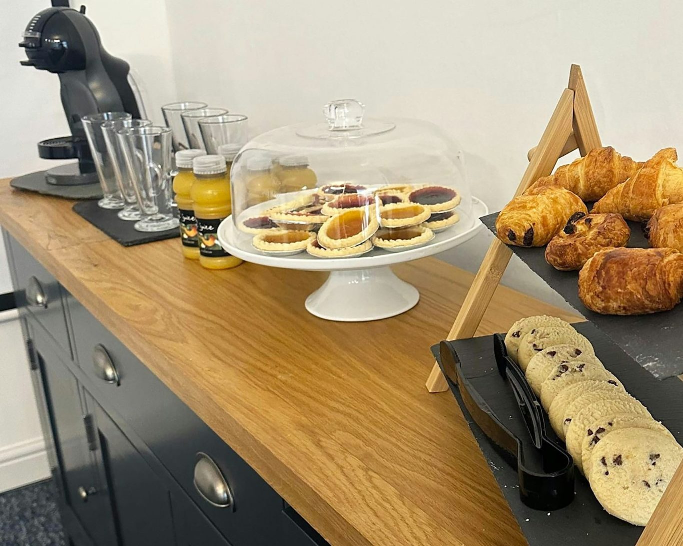 Continental breakfast spread with croissants, cookies, juice, and coffee station on wooden counter.