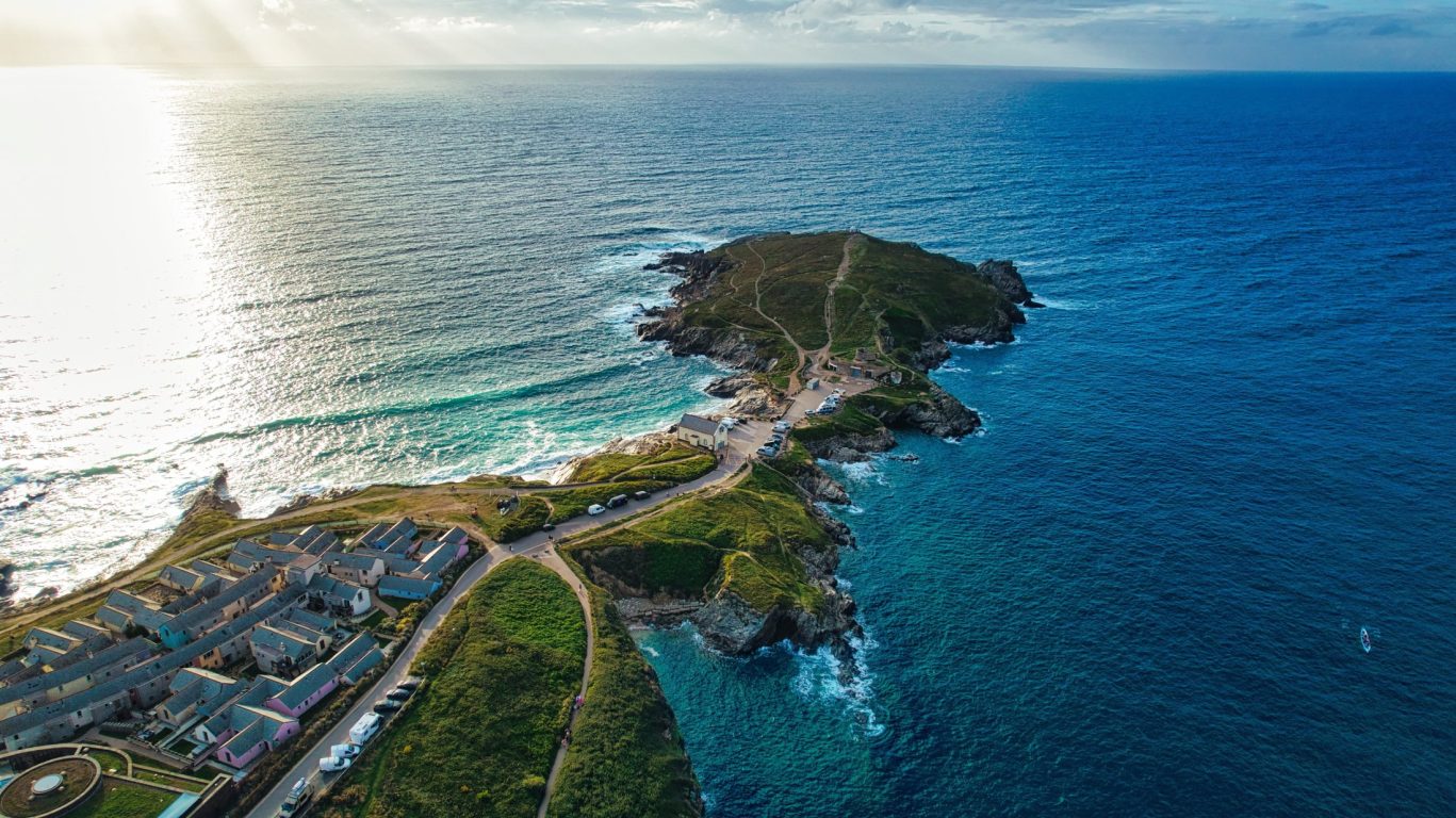 Stunning aerial view of a coastal headland surrounded by ocean with walking paths and buildings.