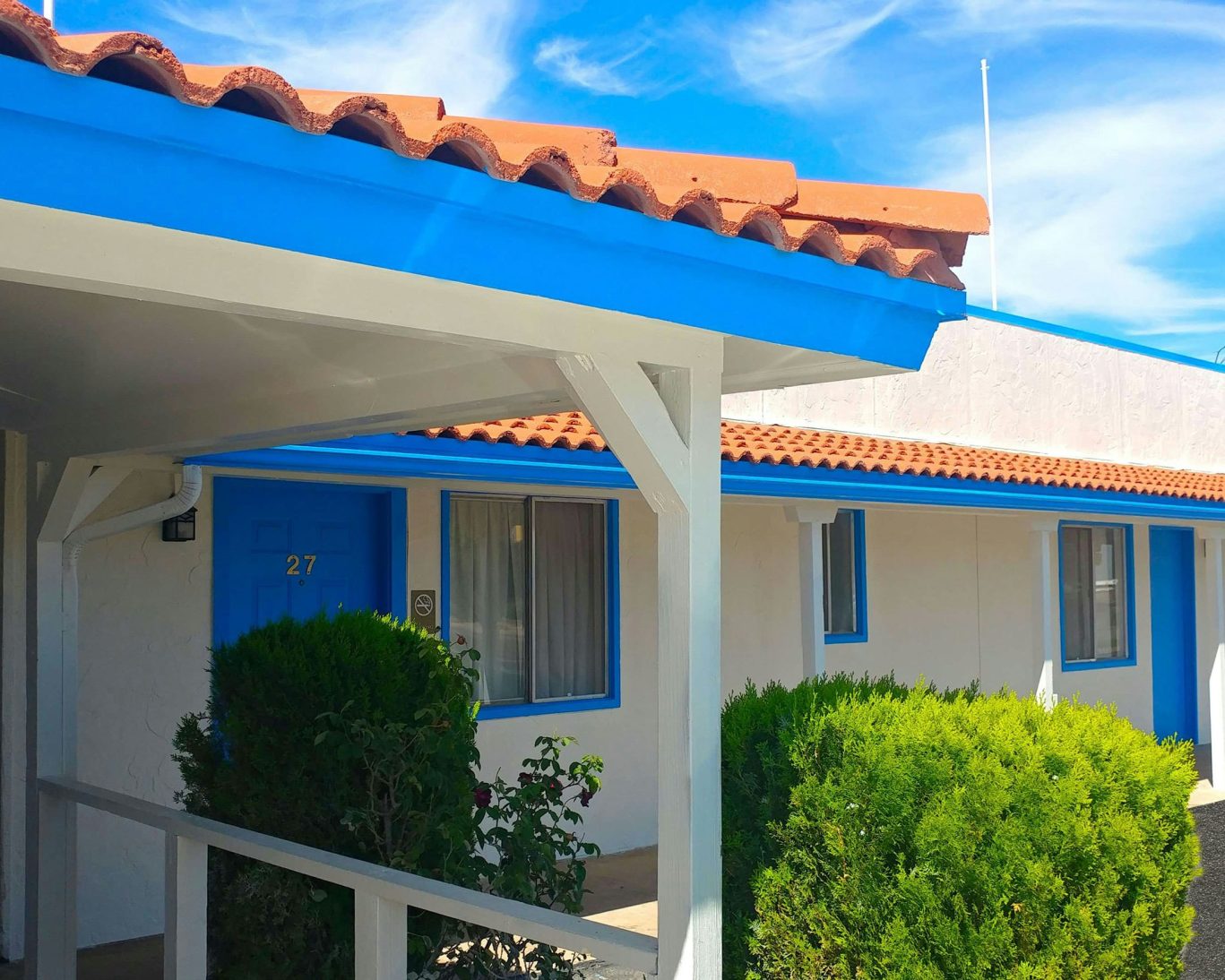Exterior view of guest room at Magnuson Hotel Sierra Vista with bright blue trim, red tile roof, and desert landscaping.