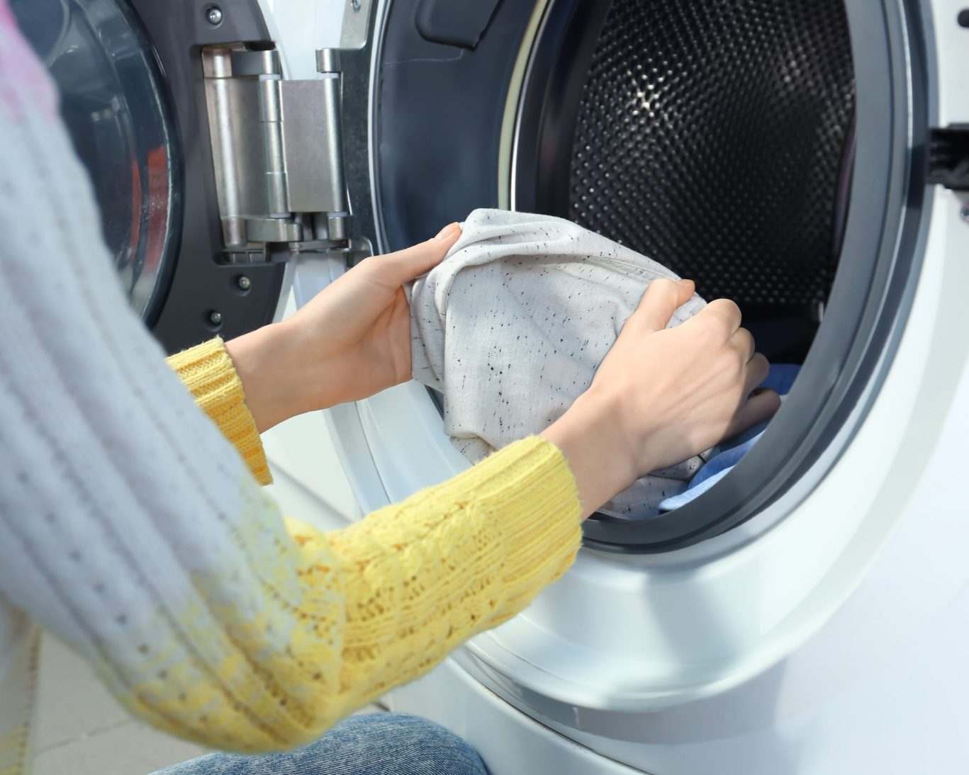 Woman loading clothes into a front-loading washing machine, demonstrating laundry service or self-service facility.