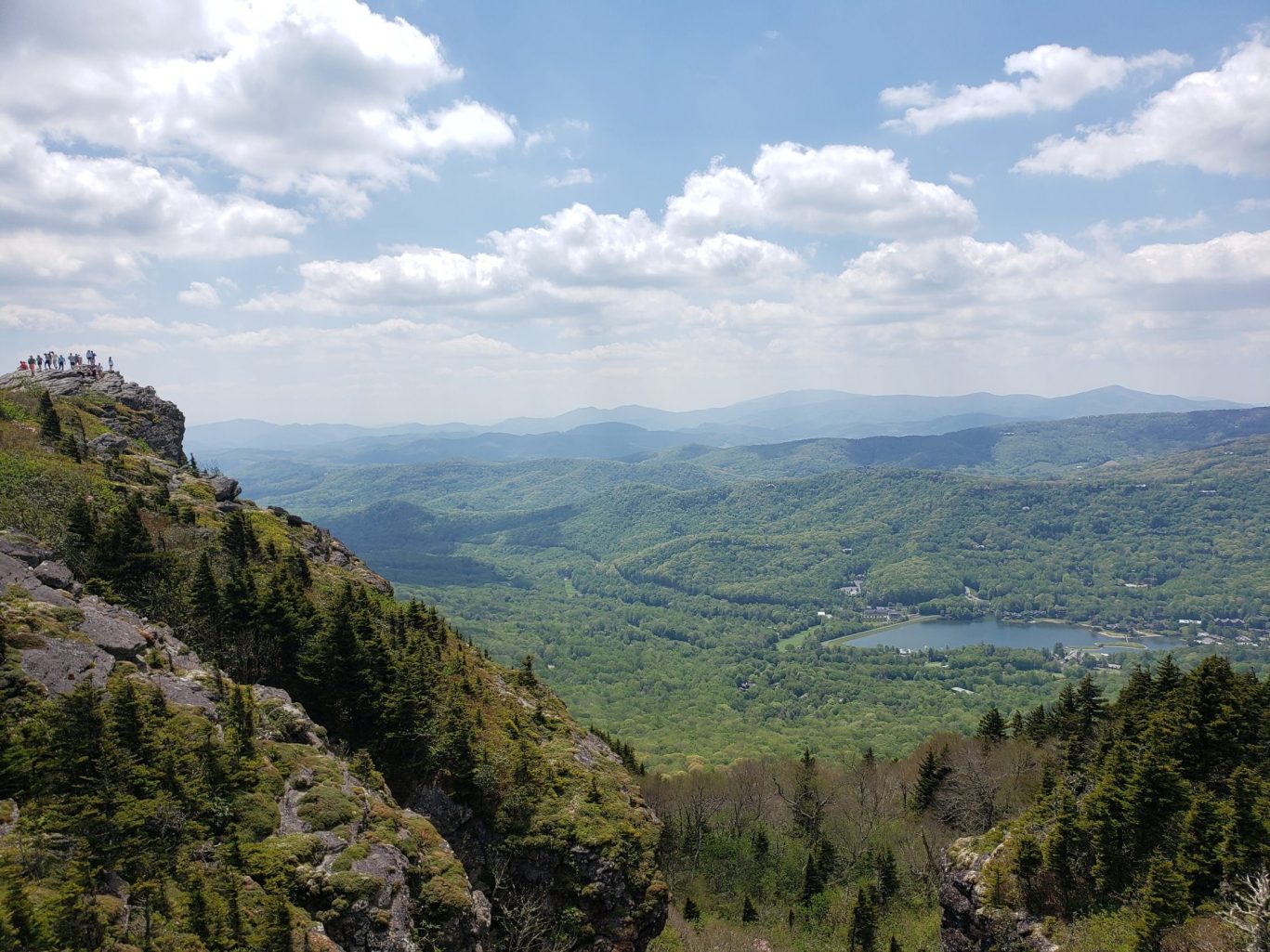 Hikers on rocky summit overlook with panoramic views of Blue Ridge Mou.ntains and forested valley in North Carolina
