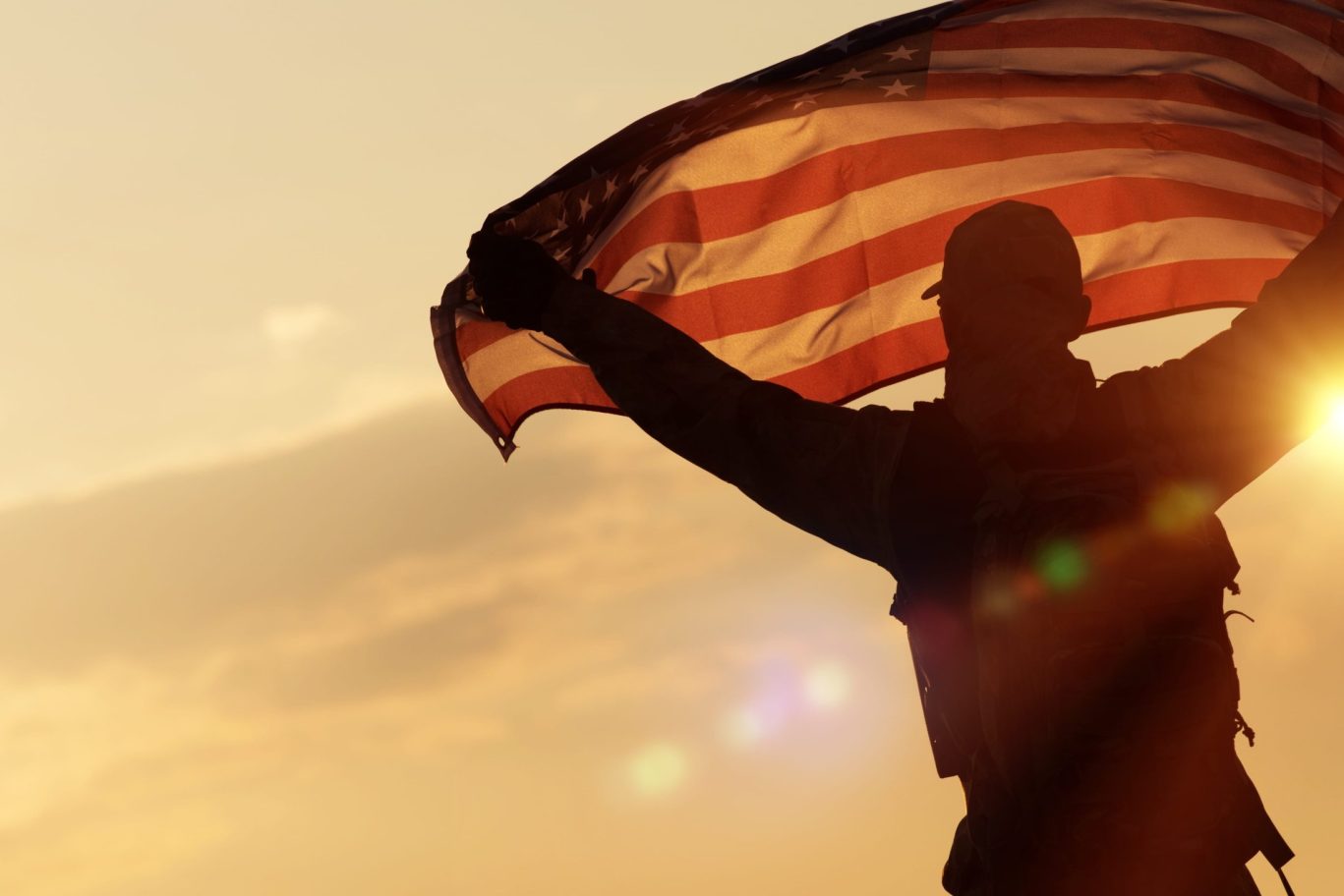 Silhouette of military soldier holding American flag during sunset with lens flare.